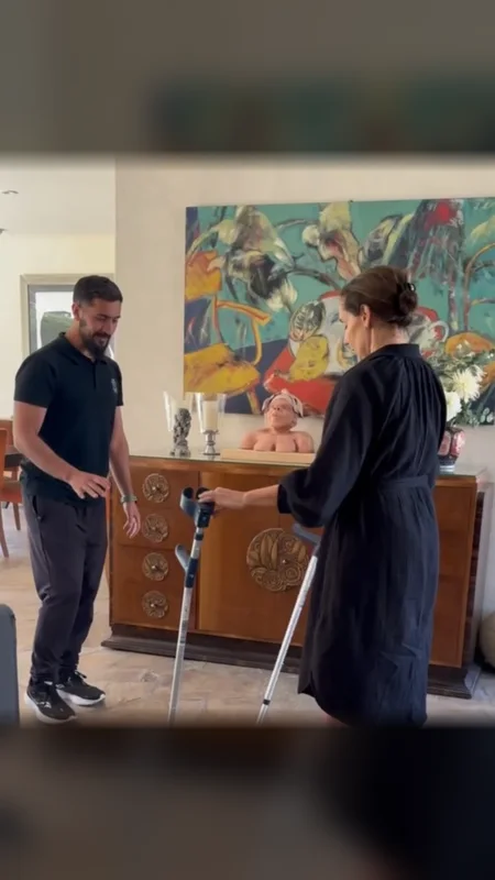 Federico Diedrichs acompaña a una clienta que camina con bastones en el living de su casa