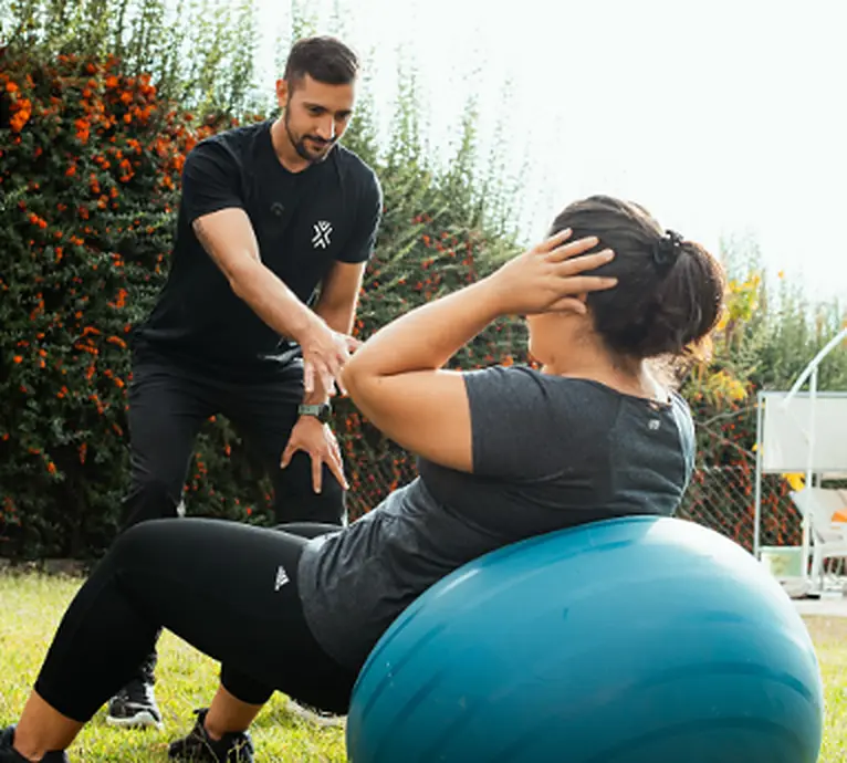 Federico Diedrichs guía a una clienta en un ejercicio de abdominales sobre una pelota en el jardín